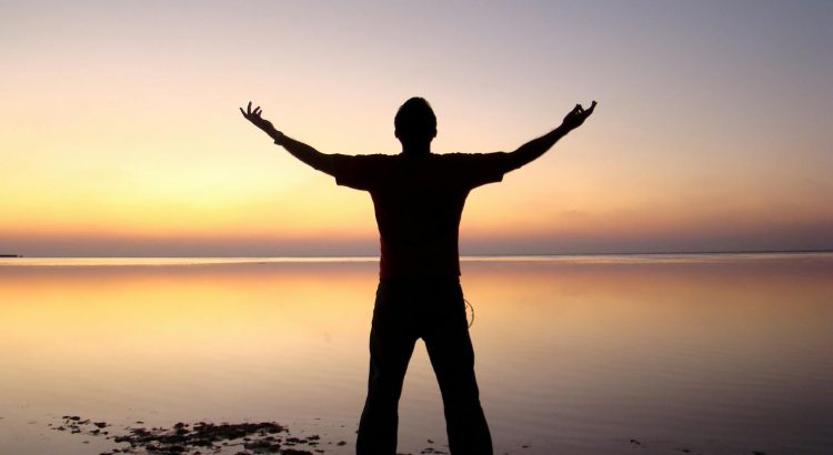 silhouette of man standing beside ocean during sunset